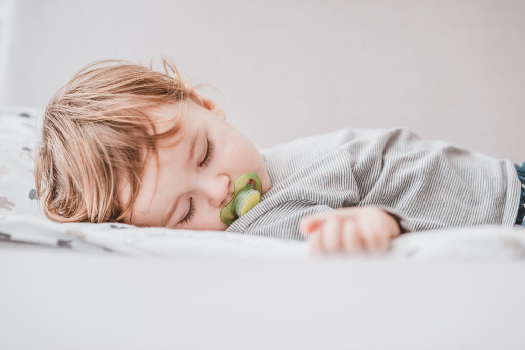 Photo of One year old baby boy sleeping during the day. Baby sleeping with open arms and with pacifier. Daytime sleep of the child.