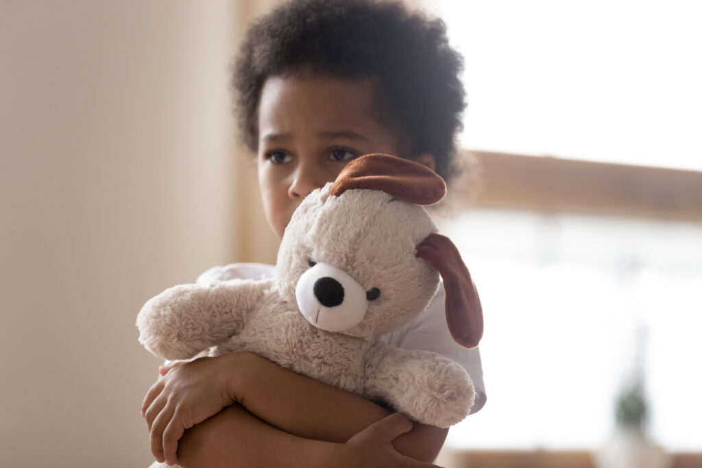 Unhappy mixed race little boy stand hugging stuffed teddy bear feel lonely lacking attention or communication, hurt small biracial kid hold plush toy suffer from loneliness, need parents