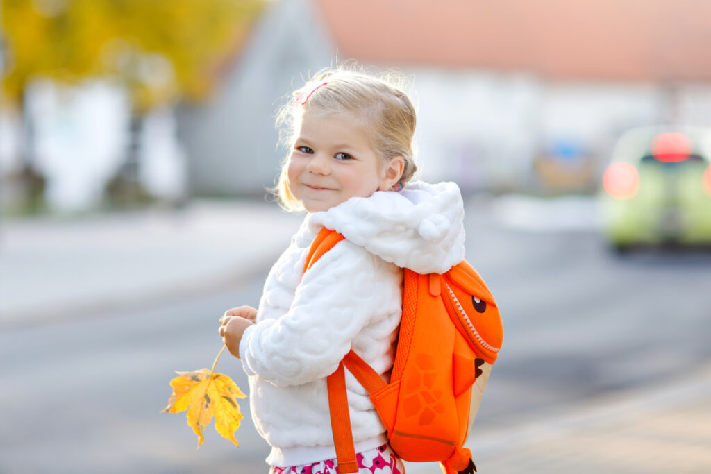 Cute little adorable toddler girl on her first day going to playschool. Healthy happy baby walking to nursery school. child with backpack going to day care on the city street, outdoors.