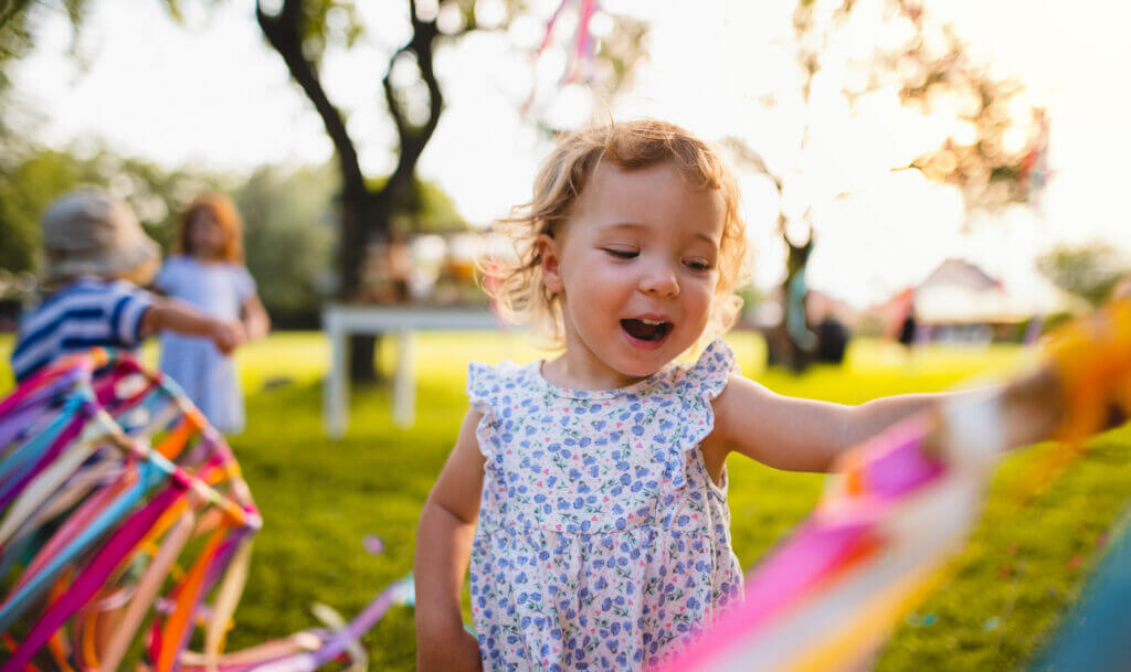 A front view of small toddler girl on birthday party outdoors in garden in summer.