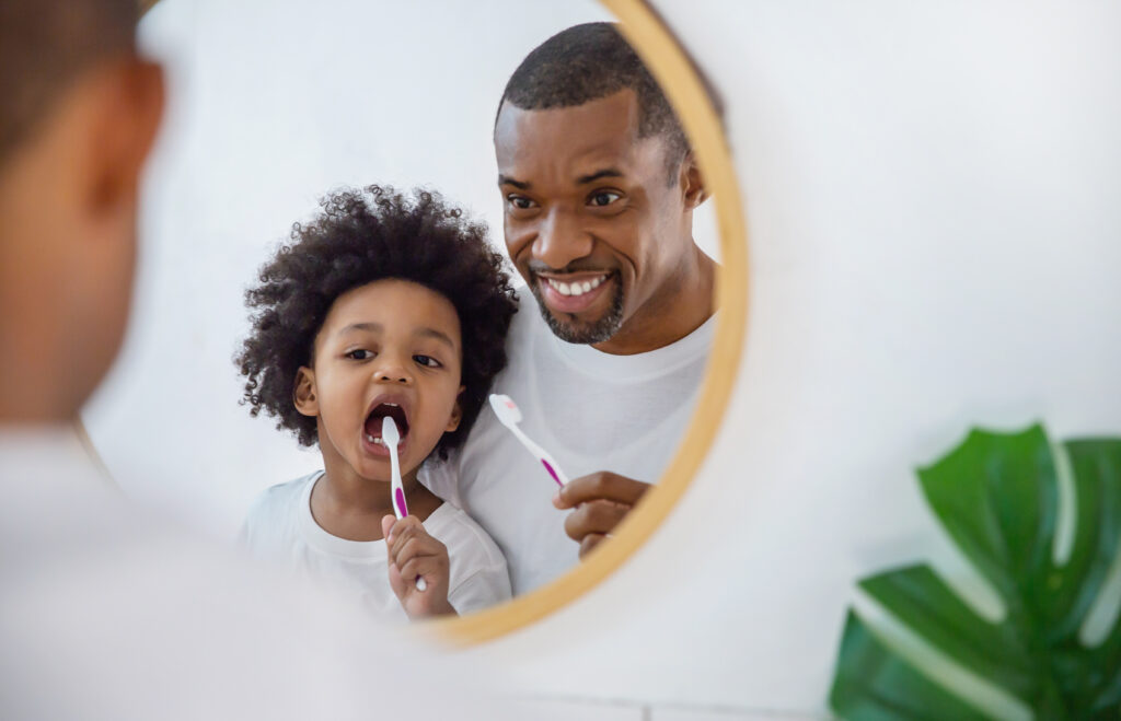 Father helping his toddler brush his teeth