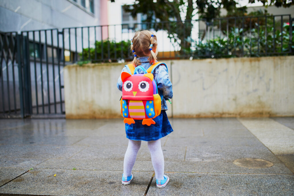 Adorable toddler girl with funny backpack ready to go to daycare, kindergarten or school. First day of school concept