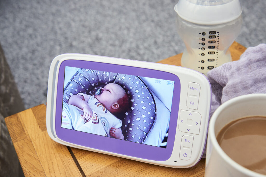A parent sat on the couch looking at the baby monitor while having a cup of tea.