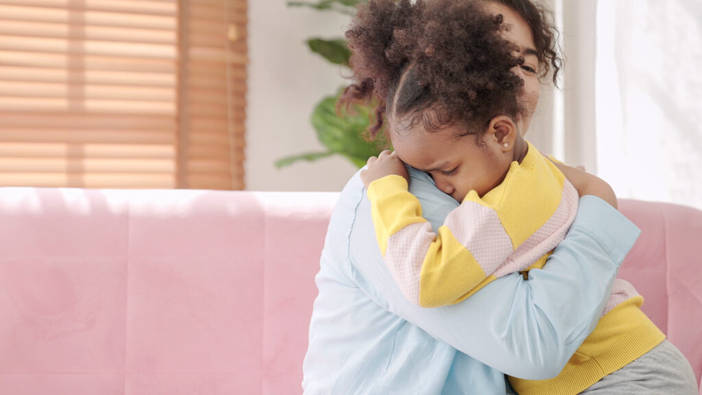 Mother consoling a crying little child and hugging little daughter. Offended black little girl crying on sofa comforting small daughter in the arms of a parent. children psychologist concept