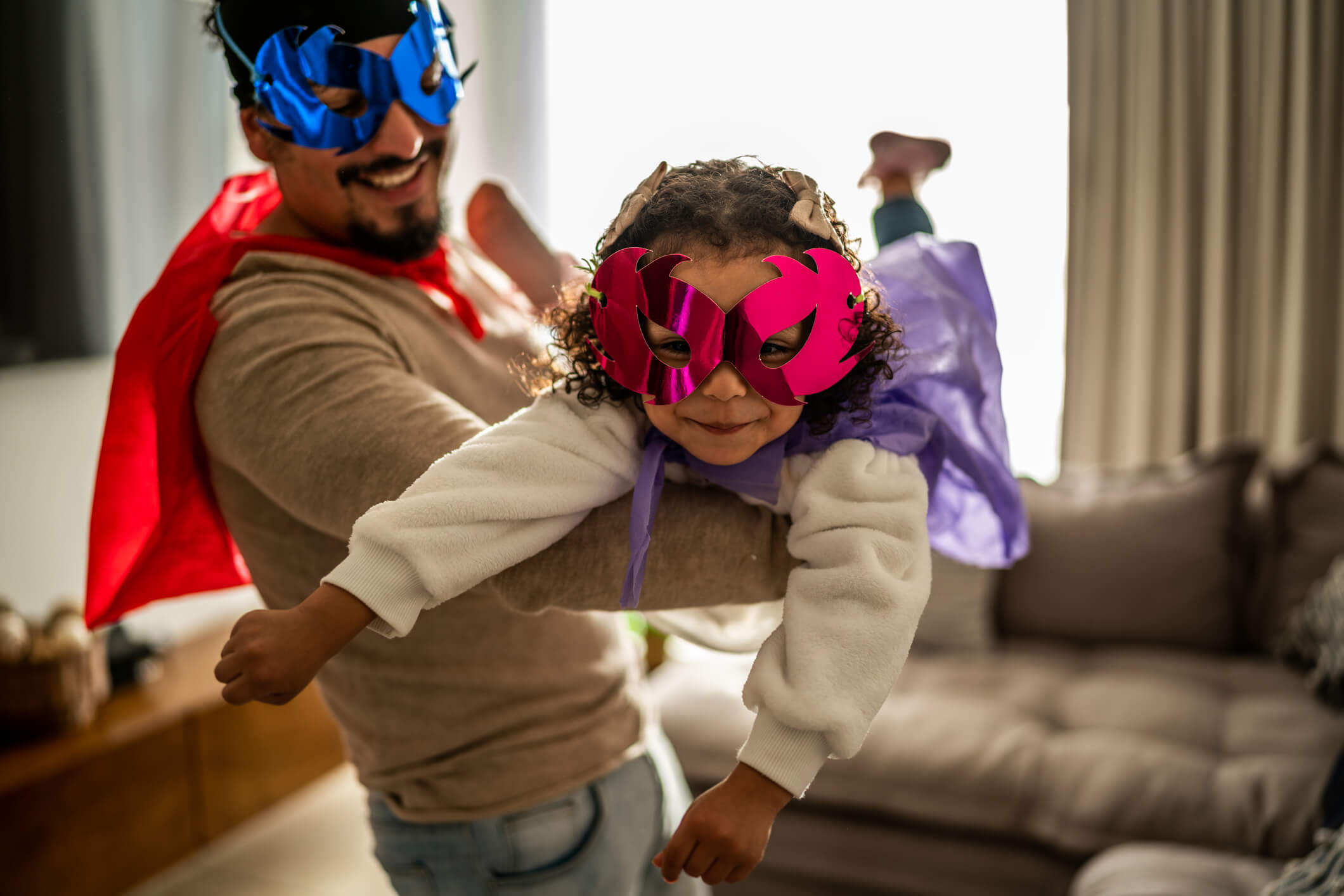 Portrait of father and daughter playing superhero in the living room at home