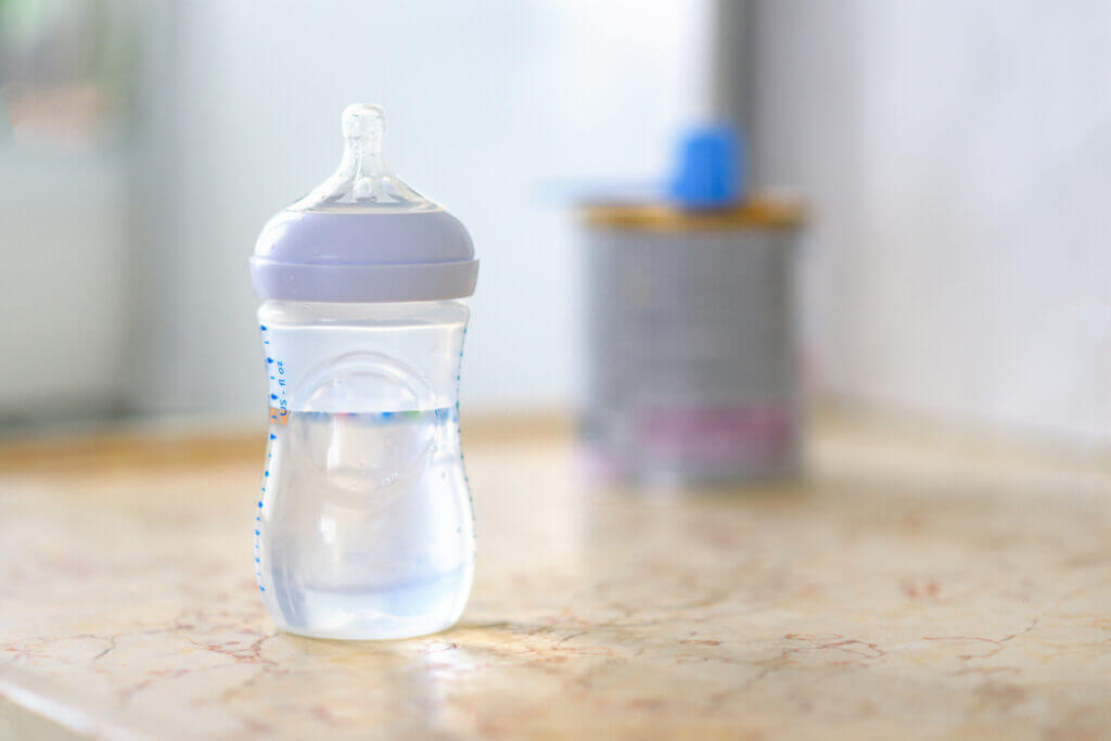 Preparation of mixture baby feeding on marble background in morning kitchen. Feeding bottle with water and baby milk formula with spoon on table.Selective focus.
