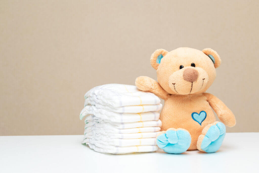 Stack of diapers with toy teddy bear on table. set for boy girl for baby shower with copy space.