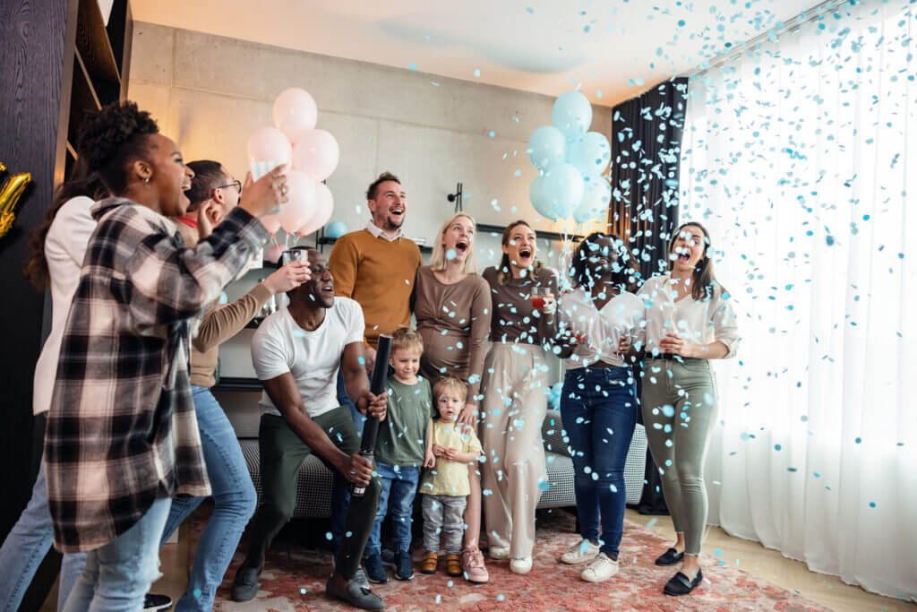 A diverse group of friends popping the confetti cannon to reveal the expectant couple is having a baby boy. They are smiling, cheering, and celebrating together this memorable moment. The gender reveal party is located in a modern apartment with cute baby shower decorations.