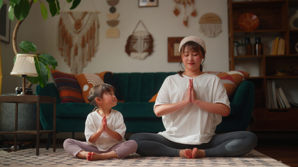 A mother and her small daughter are bonding and practicing yoga in the living room at home.