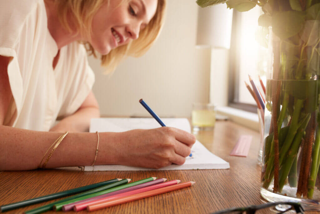 Close up of relaxed woman coloring an adult coloring book with pencils, she is sitting on a table at home.