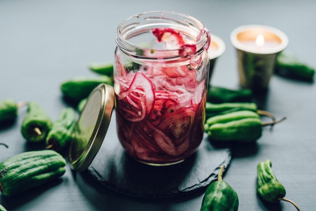 Pickled onions in a jar next to peppers on a countertop