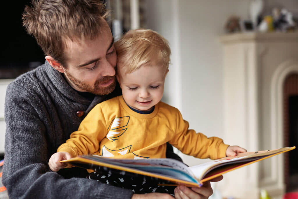 Cropped shot of an adorable little boy reading a book while sitting with his father at home