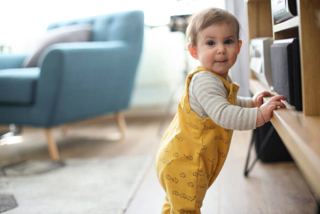 Baby girl making her first steps alone with support from furniture in the living room